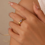 Close-up of a hand wearing a gold ring with a heart-shaped gemstone on a beige background