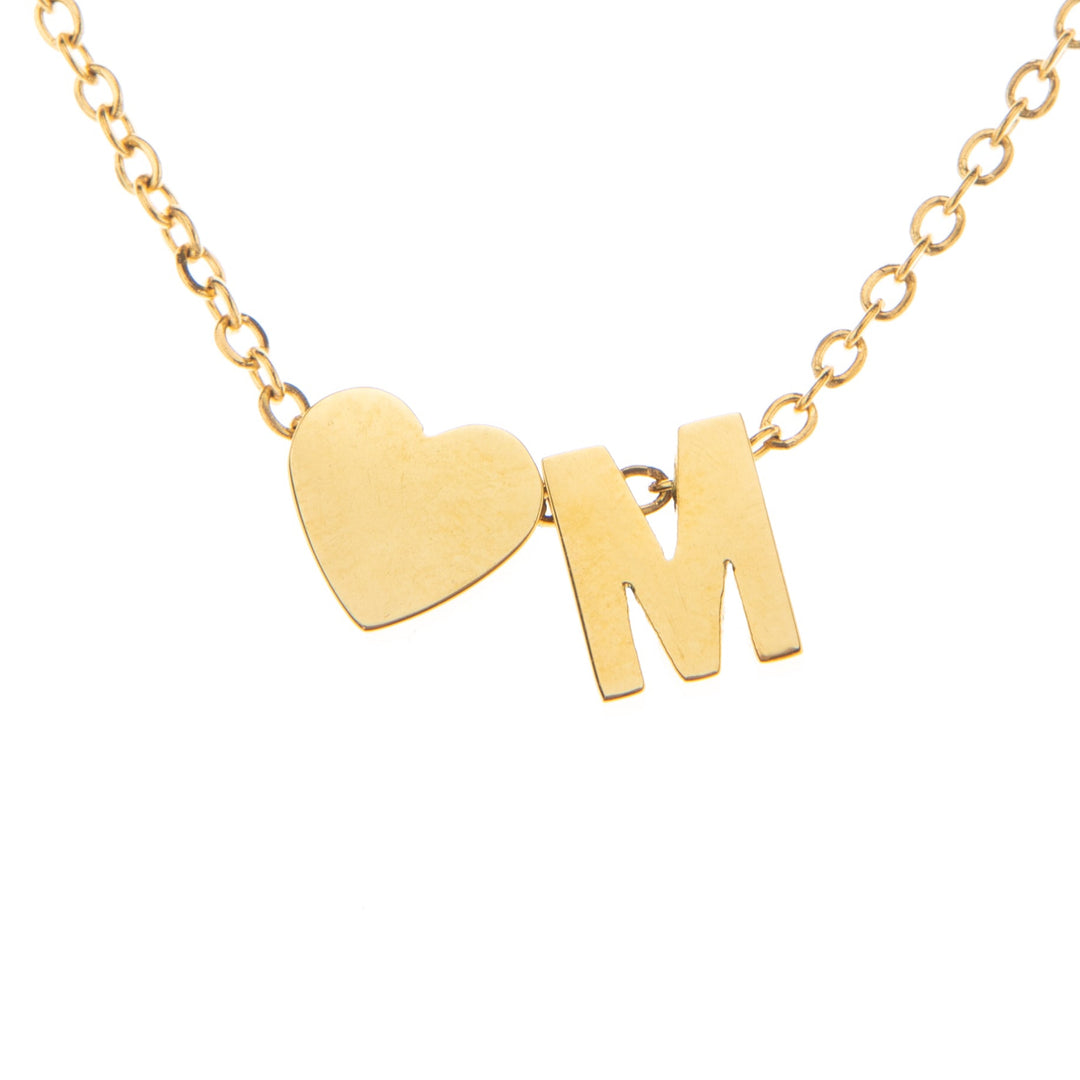 A gold-colored necklace with a heart-shaped pendant featuring the initial 'M' in the center.